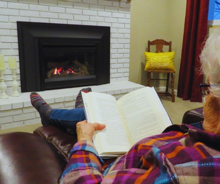 Woman sitting in her living room reading a book by a running propane fireplace